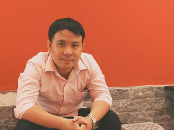 Portrait of young man sitting against orange wall