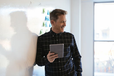 Smiling businessman with tablet in office leaning against whiteboard