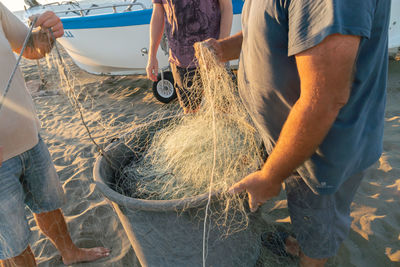 Midsection of people holding fishing net at beach