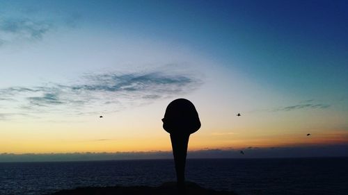 Silhouette bollard by sea against sky during sunset