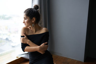 Woman looking away while standing against wall