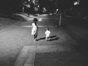 Rear view of girl walking with brother on footpath at night