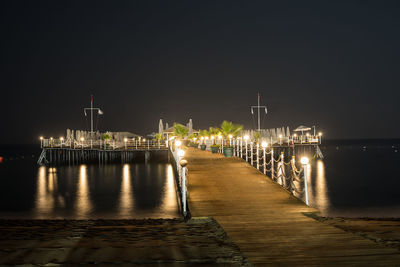 Illuminated pier over sea against sky at night