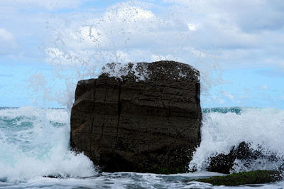 Sea waves splashing on rocks against sky
