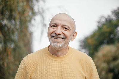 Joyful elderly man in yellow sweater laughing in a verdant urban setting