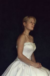 Young woman with arms raised standing against black background