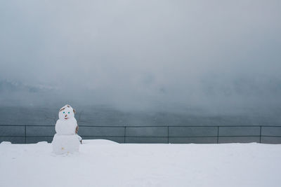 Snowman on snow covered field by railing during foggy weather