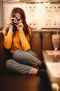 Teenage girl photographing with vintage camera while sitting in cafe