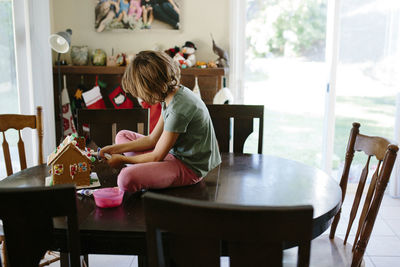 Girl making gingerbread house on table at home