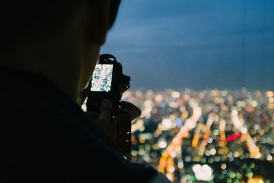 Rear view of person photographing illuminated cityscape against sky at dusk