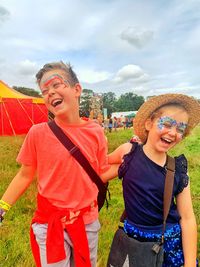 Smiling siblings standing against sky