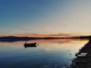 Silhouette boat in lake against sky during sunset