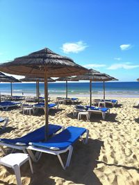 Chairs on beach by sea against blue sky