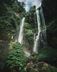 Low angle view of young man standing against waterfall in forest