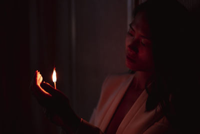 Woman looking at burning match stick in dark at home