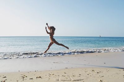 Full length of woman jumping at beach against sky