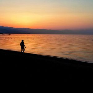 Silhouette man walking on beach against sky during sunset