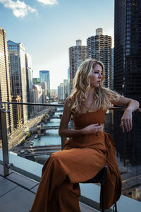 Young woman sitting against buildings in city