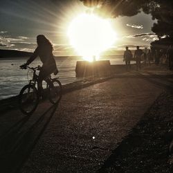 People riding bicycle on beach against bright sun