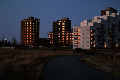 Illuminated buildings in city against clear sky at dusk