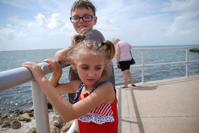 Siblings standing by railing at beach