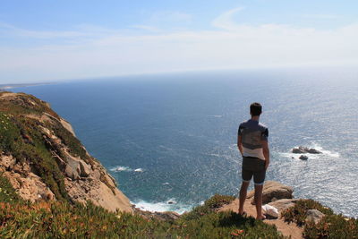 Rear view of man standing on cliff against sky