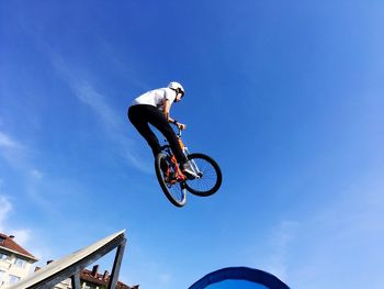 Low angle view of man jumping against blue sky