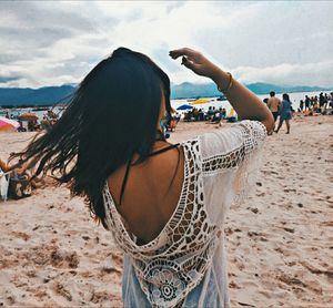 Rear view of woman standing at beach against cloudy sky