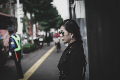 Portrait of young woman looking away while standing on road in city