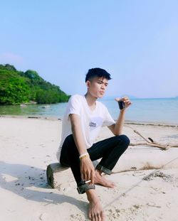 Portrait of young woman sitting on beach against clear sky