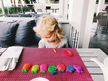 Cute girl playing with colorful clay on table at home