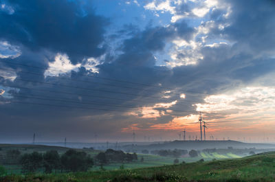 Electricity pylon on field against dramatic sky