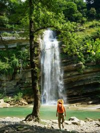Rear view of woman standing by waterfall in forest