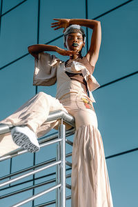 Low angle view of young woman standing against windows 