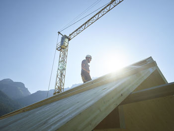 Carpenter standing on roof at construction site under clear sky