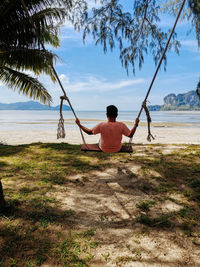 Rear view of man sitting on beach against sky