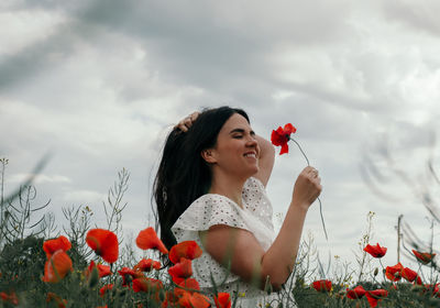 Portrait of beautiful young woman wearing white dress, standing in poppy field