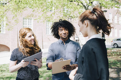 Confident businesswoman discussing with multi-ethnic colleagues while standing outdoors