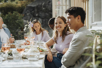 Portrait of smiling young woman sitting with friends during dinner party at cafe