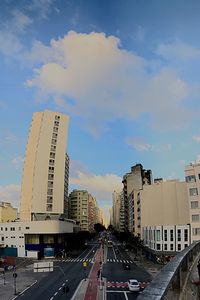 Cars on road by buildings against sky in city