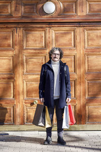 Man with shopping bags standing in front of wooden door on sunny day