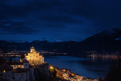 Illuminated buildings by lake against sky at night