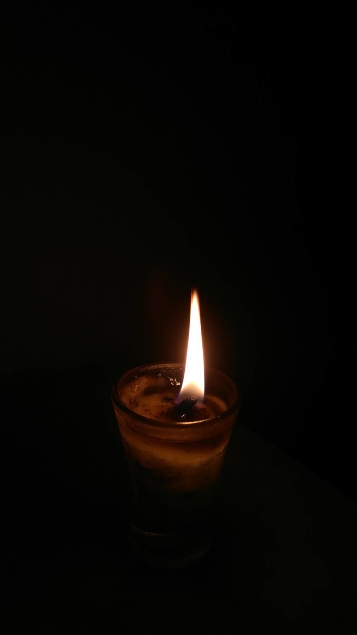 CLOSE-UP OF BURNING CANDLE IN DARKROOM