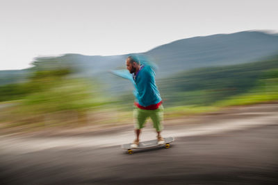 Full length of mid adult man skateboarding on mountain against sky