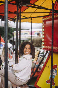 Happy girl looking over shoulder while having fun on carousel at amusement park