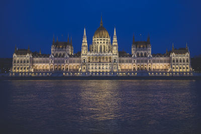 Illuminated hungarian parliament building by river against clear sky at night