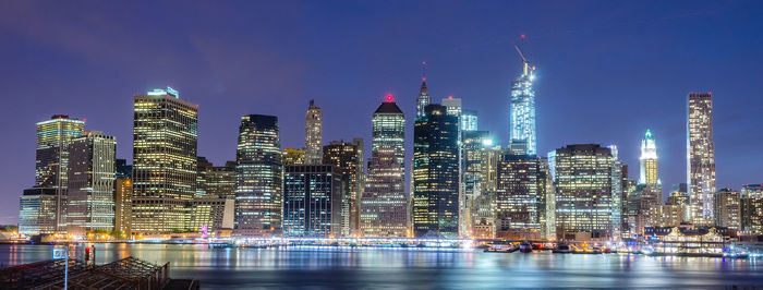 Illuminated modern buildings in city against sky at night