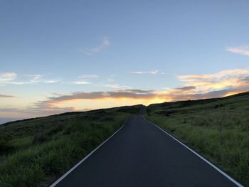 Road amidst field against sky during sunset