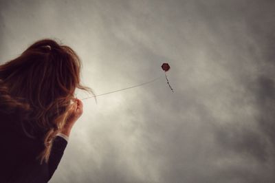 Low angle view of woman flying kite against sky