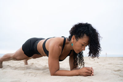 Side view of fit female athlete doing plank exercise while training on sandy shore